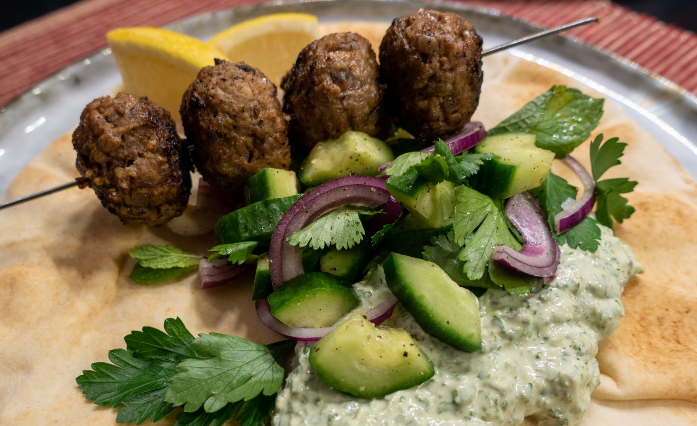 Oriental meatball skewer with kale and yoghurt dip and herb salad on a flatbread